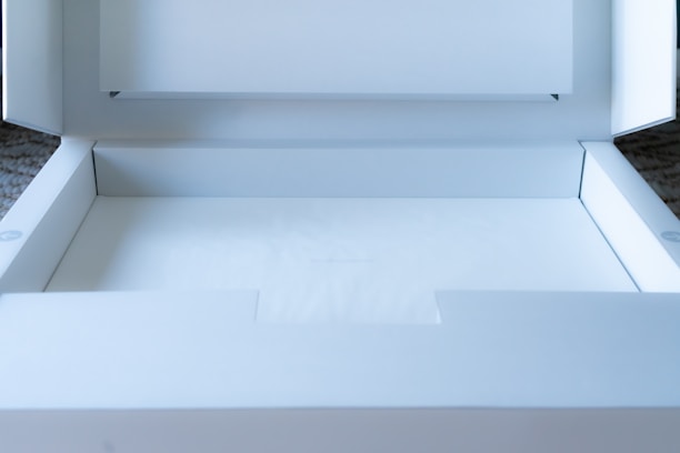 A clean, white cardboard box is open, revealing an empty interior. The box is well-lit, showing crisp edges and subtle shadows. It appears to be a package ready for use, possibly for shipping or storage.