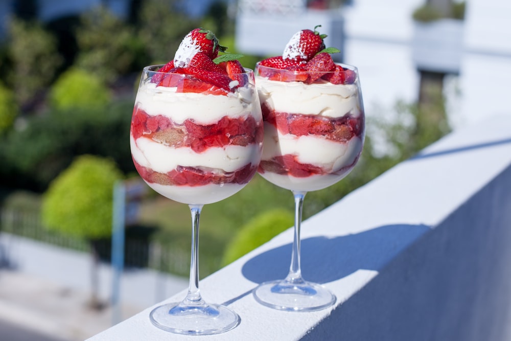 two glasses filled with dessert sitting on a ledge