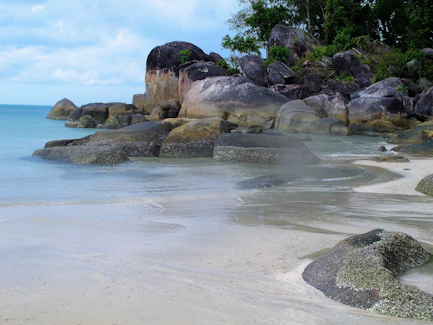 a sandy beach with large rocks and water