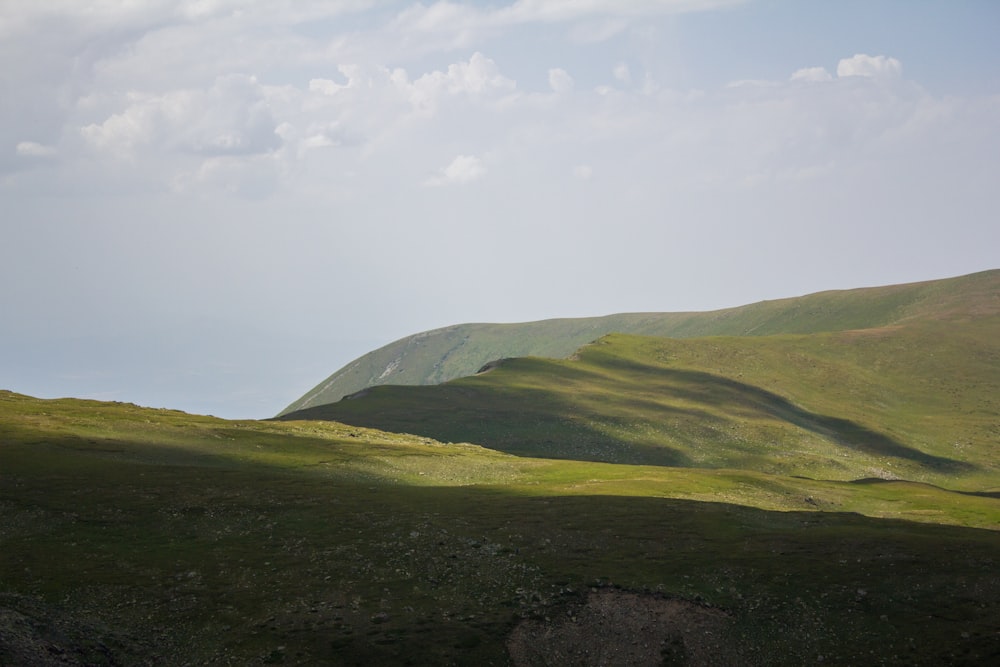 a grassy hill with a few clouds in the sky