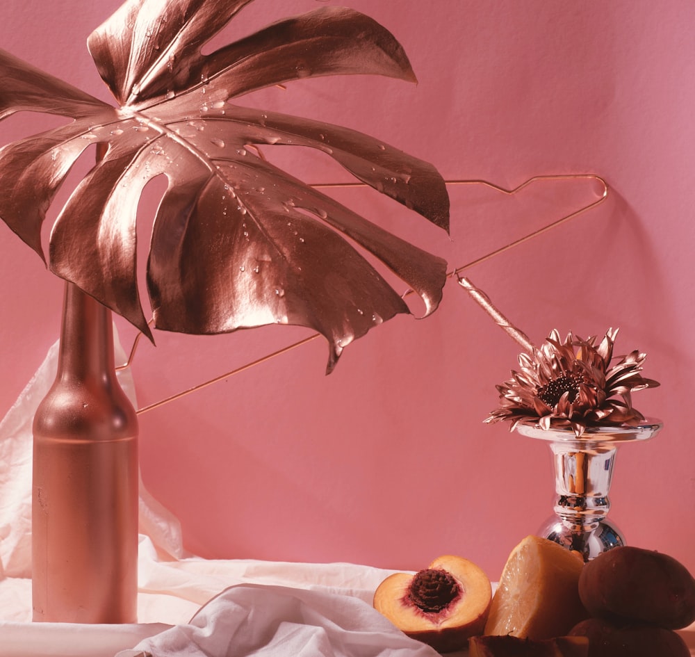 a vase with a plant and some fruit on a table