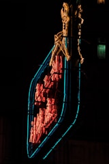 A neon sign illuminated against a dark background, featuring a stylized running deer in yellow above Chinese characters in red. The sign is encased in a distinctive geometric frame outlined with blue neon lighting.