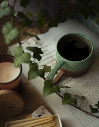 A cozy scene with hands holding a warm mug beside a softly lit candle and a journal.