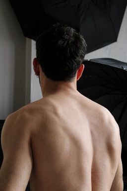 a man with no shirt standing in front of a black umbrella