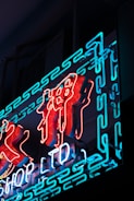 Neon sign featuring stylized characters in vibrant red and blue lights, set against a dark background. The illumination creates a bright and striking contrast.