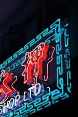 Neon sign featuring stylized characters in vibrant red and blue lights, set against a dark background. The illumination creates a bright and striking contrast.