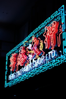 A vibrant neon sign displaying the text 'Heng Tai Pawn Shop Ltd' in English with decorative Asian characters above. The sign is illuminated with bright colors against a dark background.