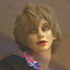 Short, chic wig with a modern cut displayed on a wooden stand in soft daylight.