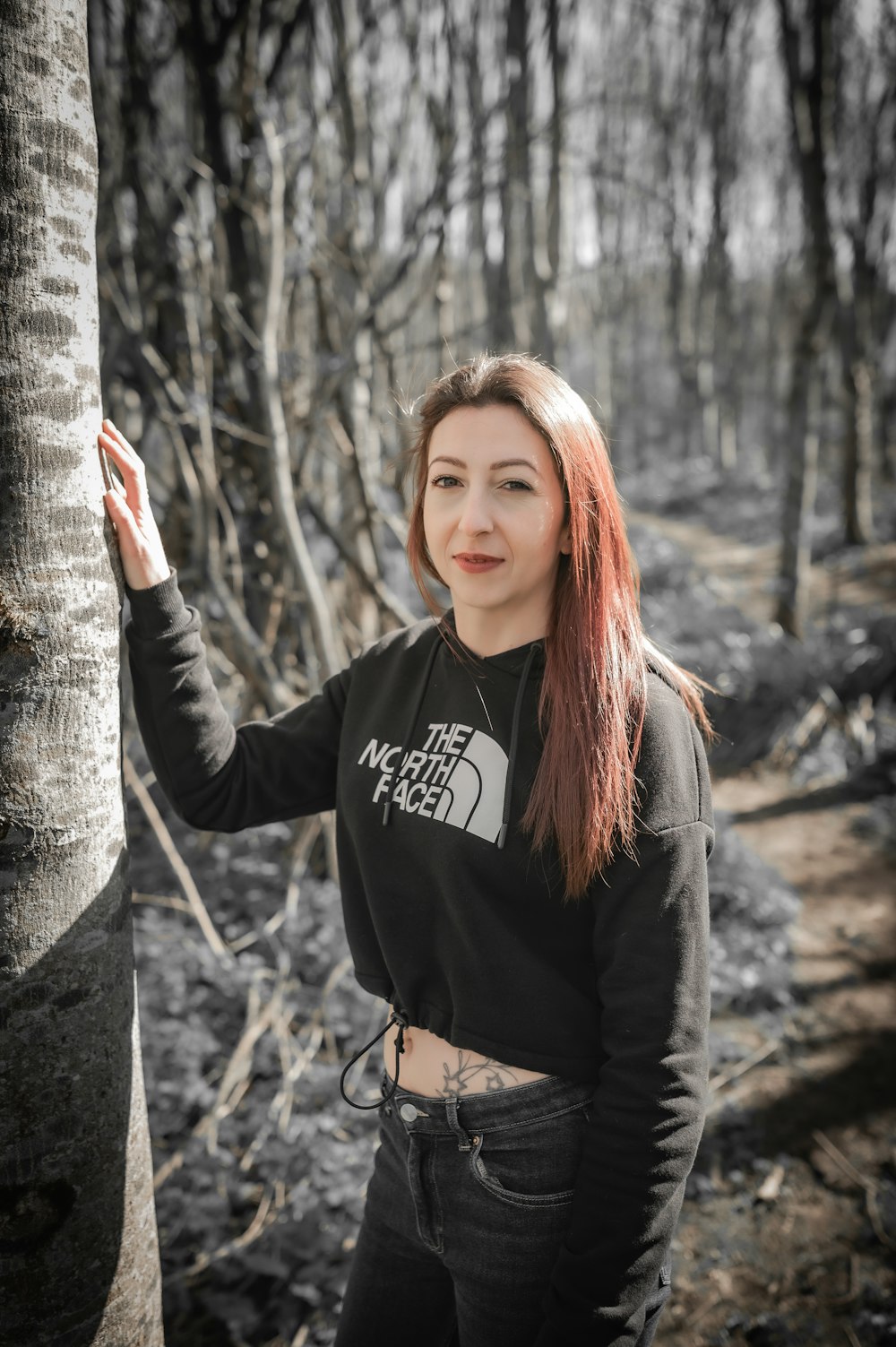 a woman standing next to a tree in a forest