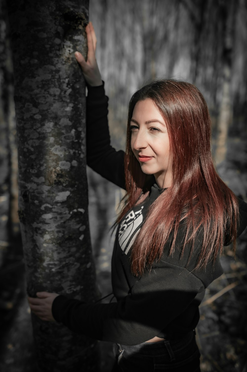 a woman standing next to a tree in a forest