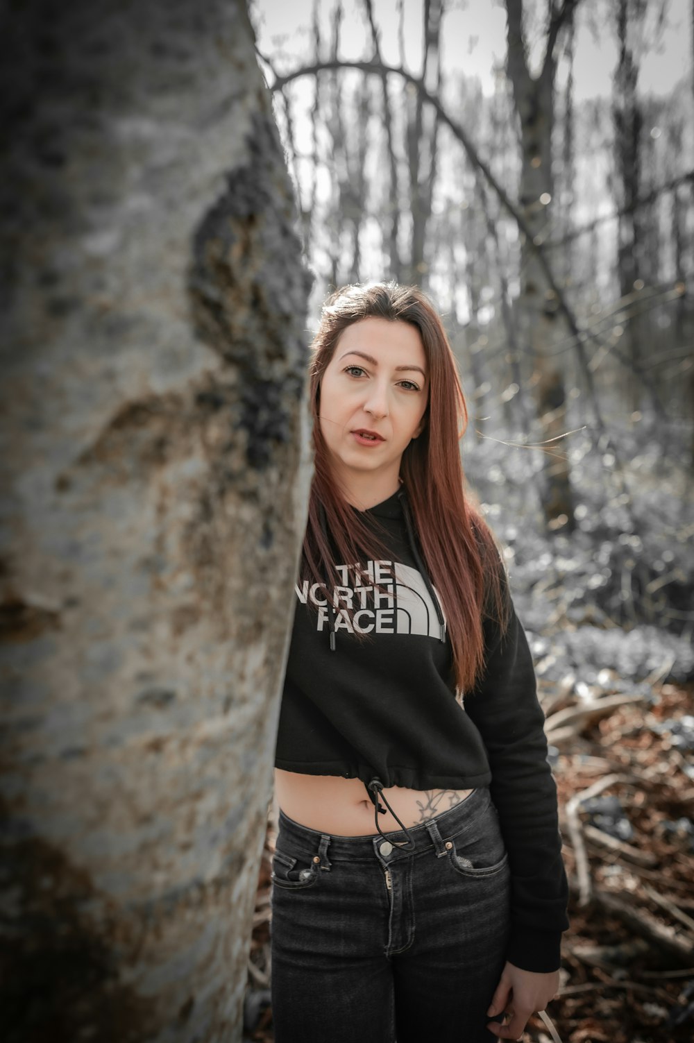 a woman standing next to a tree in a forest