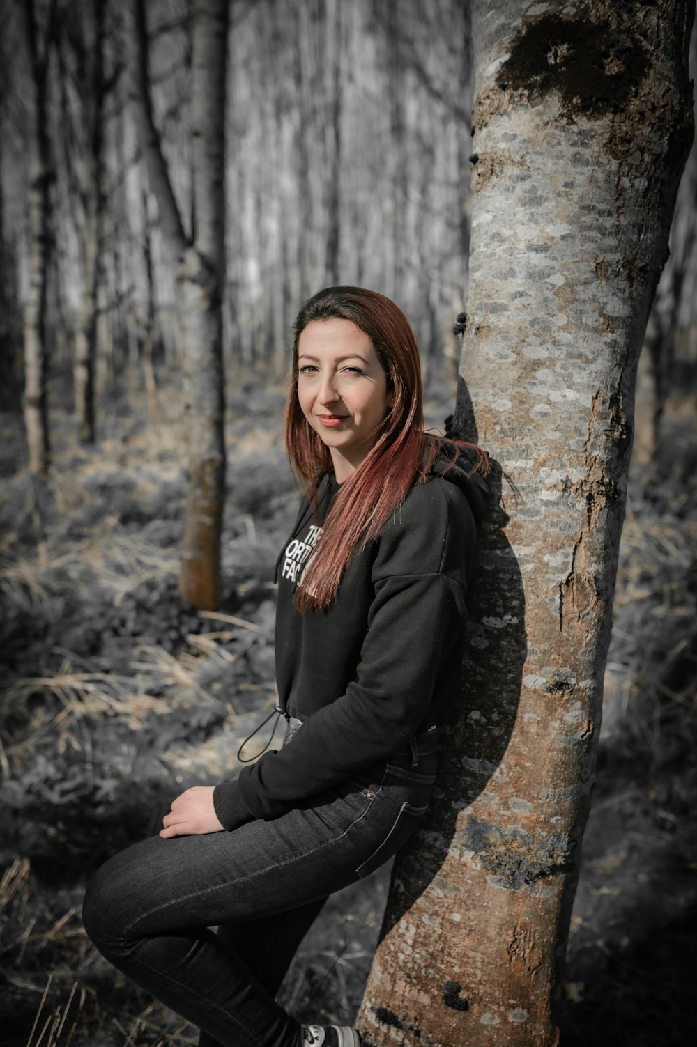 a woman sitting next to a tree in a forest