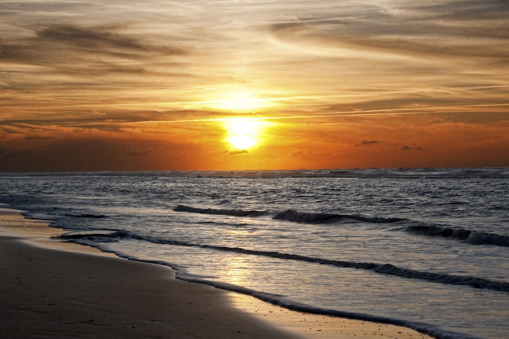 the sun is setting over the ocean on the beach