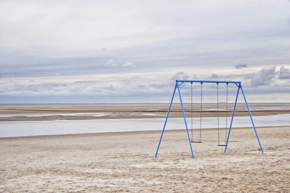 a blue swing set sitting on top of a sandy beach