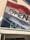 A large sign with the word 'OPEN' is displayed on a red and white flag outside a building. The building's exterior features beige paneling, and a reflective glass window beneath the flag shows a glimpse of the interior decor, including silver vases and decorative branches.