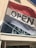 A large sign with the word 'OPEN' is displayed on a red and white flag outside a building. The building's exterior features beige paneling, and a reflective glass window beneath the flag shows a glimpse of the interior decor, including silver vases and decorative branches.