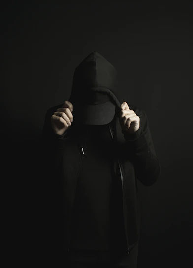 a person wearing a black hoodie and a black hat