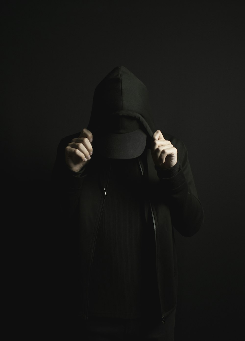a person wearing a black hoodie and a black hat