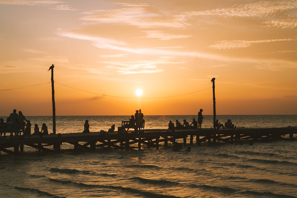 a group of people standing on a pier at sunset
