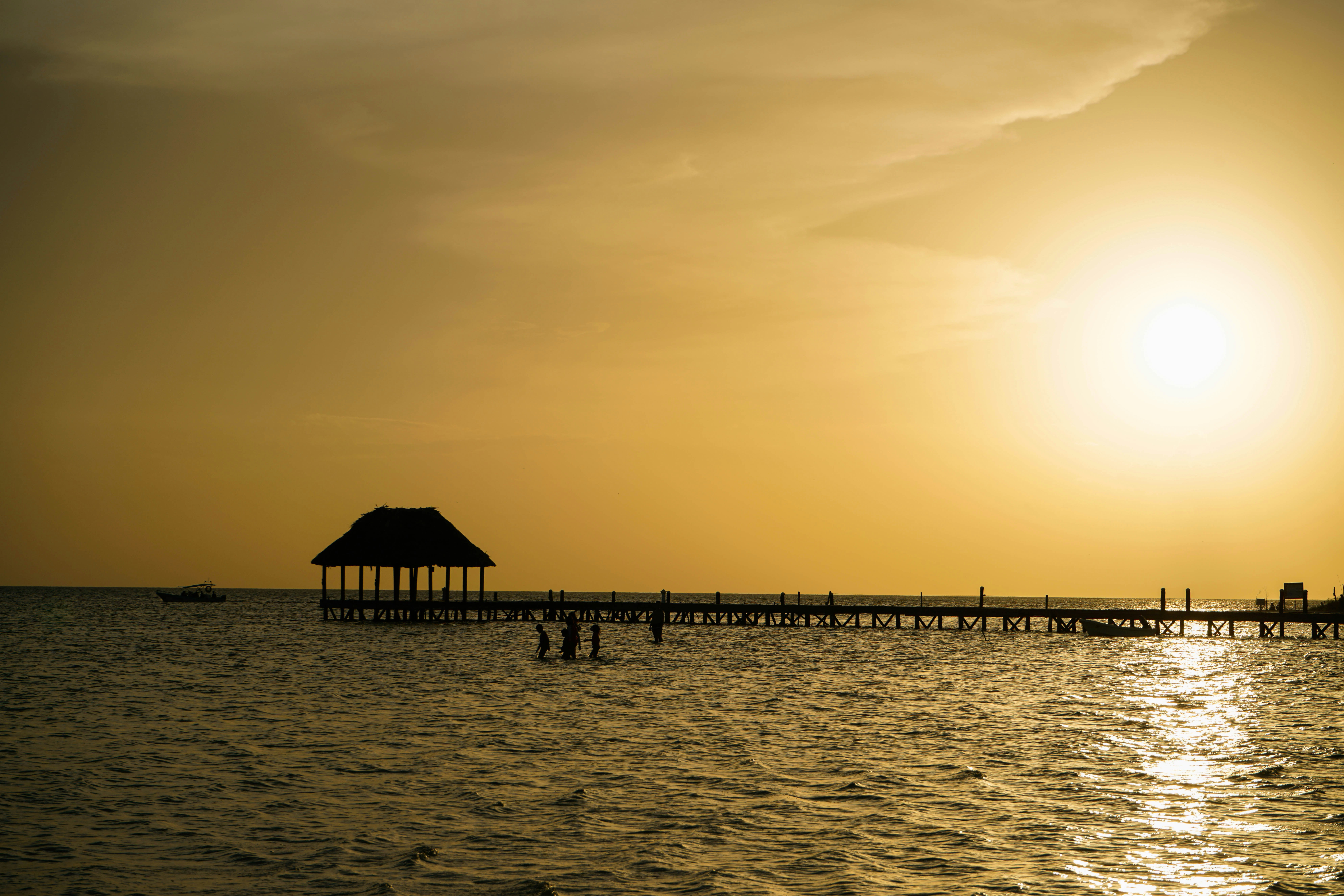 the sun is setting over the water and a pier, 