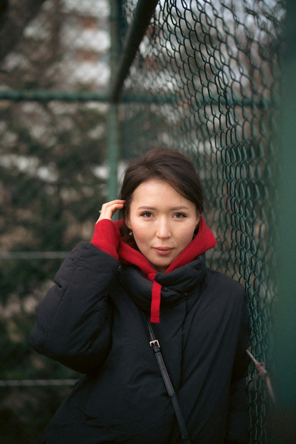 a woman in a black jacket leaning against a fence