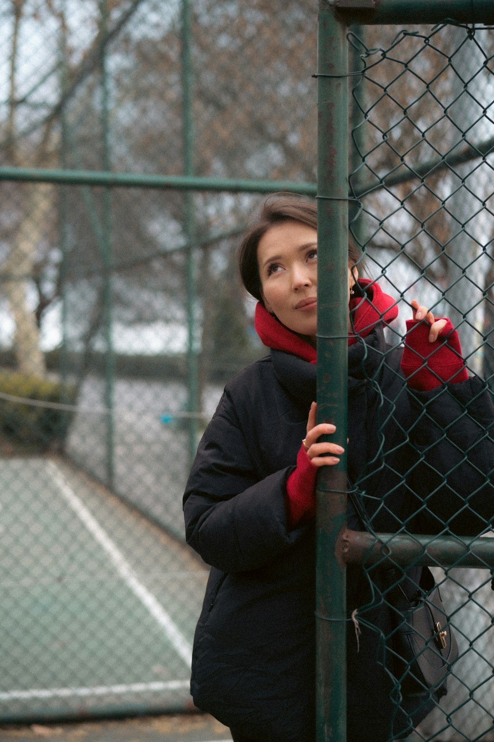 a woman leaning against a fence with a handbag