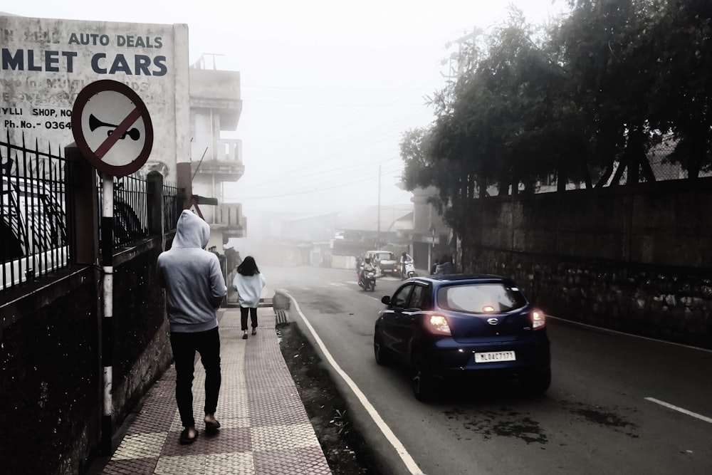 a man walking down a sidewalk next to a car