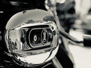 A close-up view of a polished metallic surface with curved reflections, prominently featuring an embossed emblem with the number one. The background is blurred, emphasizing the focus on the emblem and the shiny texture.