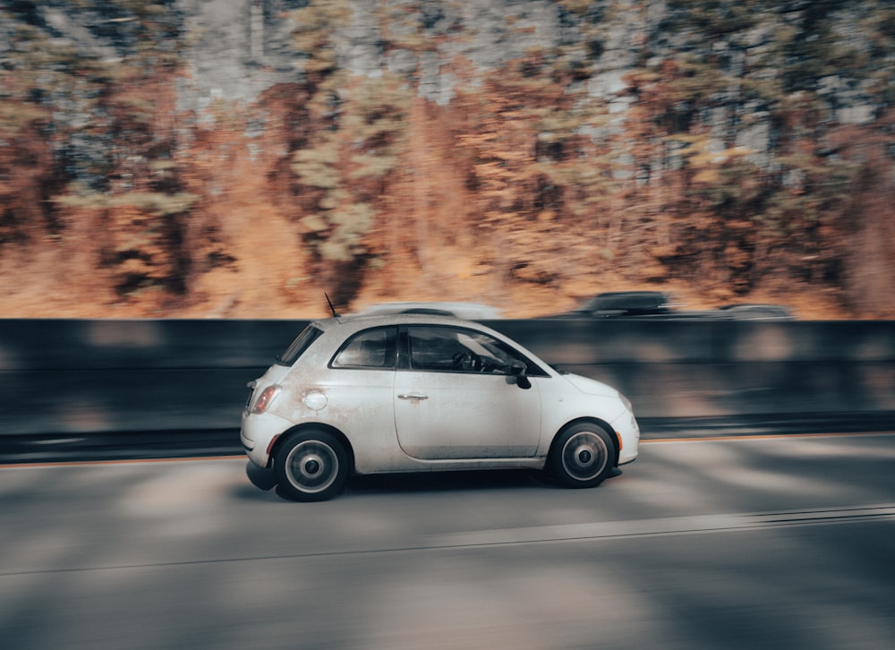 a small white car driving down a street