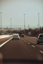A convoy of cars traveling smoothly on a highway under a clear blue sky.