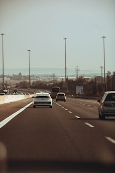 A convoy of cars traveling smoothly on a highway under a clear blue sky.