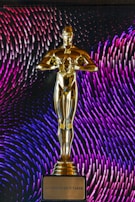 A golden statuette stands prominently on a base with an inscription that reads 'Do Whatever It Takes.' In the background, vibrant patterns of purple and blue lines create a dynamic and colorful backdrop.