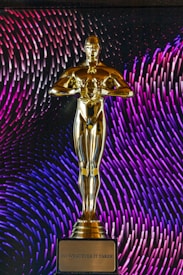 A golden statuette stands prominently on a base with an inscription that reads 'Do Whatever It Takes.' In the background, vibrant patterns of purple and blue lines create a dynamic and colorful backdrop.