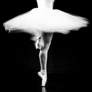 A dancer in motion captured mid-pirouette, highlighting the elegance and fluidity of ballet. The blurred tulle skirt and pointed toes suggest a dynamic and graceful movement against a dark background.