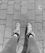 A pair of legs in leggings is visible, wearing sneakers with fur trim, standing on a paved brick pathway. The image is in black and white.
