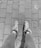 A pair of legs in leggings is visible, wearing sneakers with fur trim, standing on a paved brick pathway. The image is in black and white.