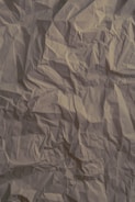 Crinkled beige paper with visible creases and folds throughout the surface, creating a textured and slightly shadowed appearance.