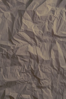 Crinkled beige paper with visible creases and folds throughout the surface, creating a textured and slightly shadowed appearance.