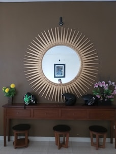 A stylish entryway featuring a sculptural mirror above a wooden console table adorned with artisan pottery and a leather catchall tray.