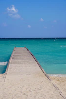 A wooden pier stretching into the crystal-clear blue sea under a bright sunny sky.