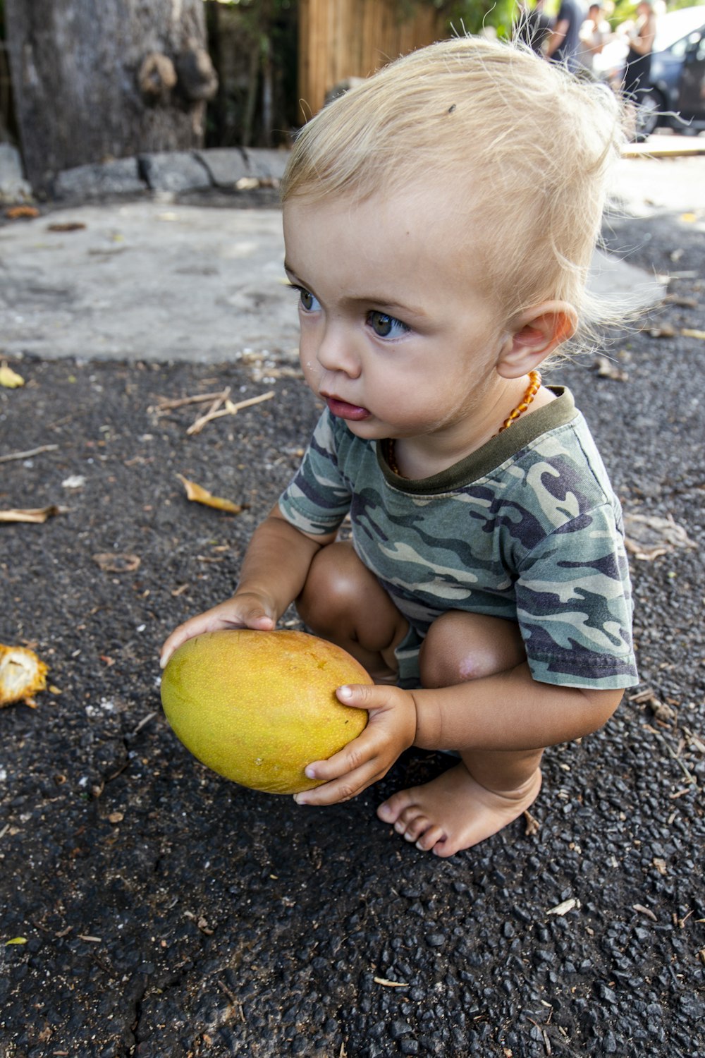a little boy sitting on the ground holding a fruit