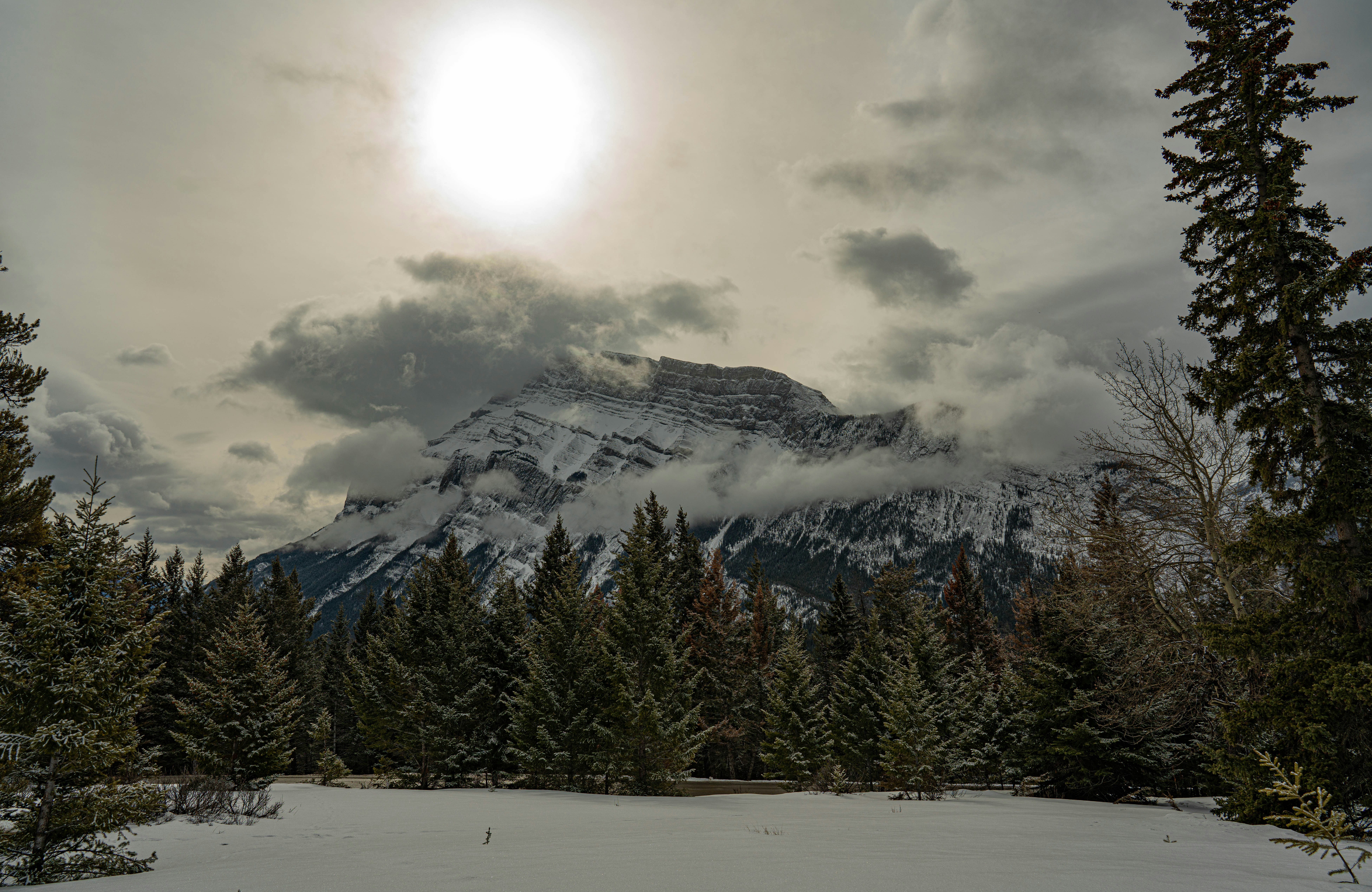 the sun shines through the clouds over a snowy mountain