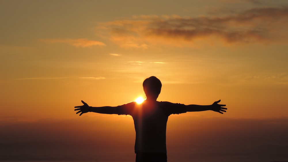 a man standing in front of the sun with his arms outstretched