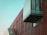 A modern architectural structure with a combination of red vertical panels and large glass windows. The building features an angular glass facade and a prominent overhanging section, creating a dynamic and contemporary design.