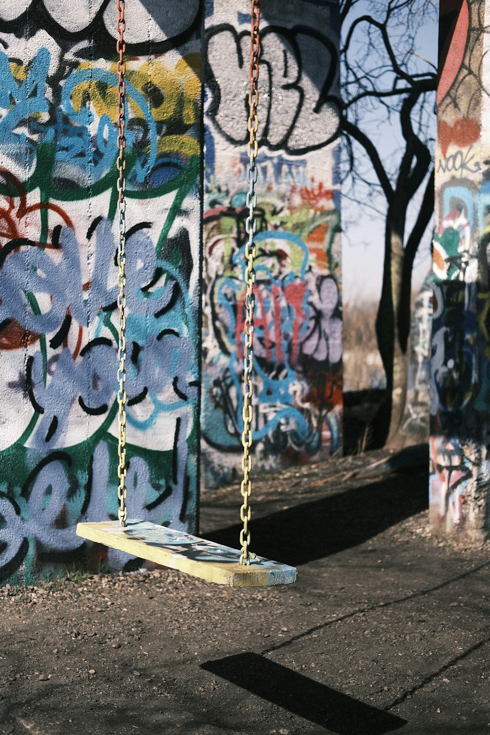 a wooden swing sitting in front of a graffiti covered wall