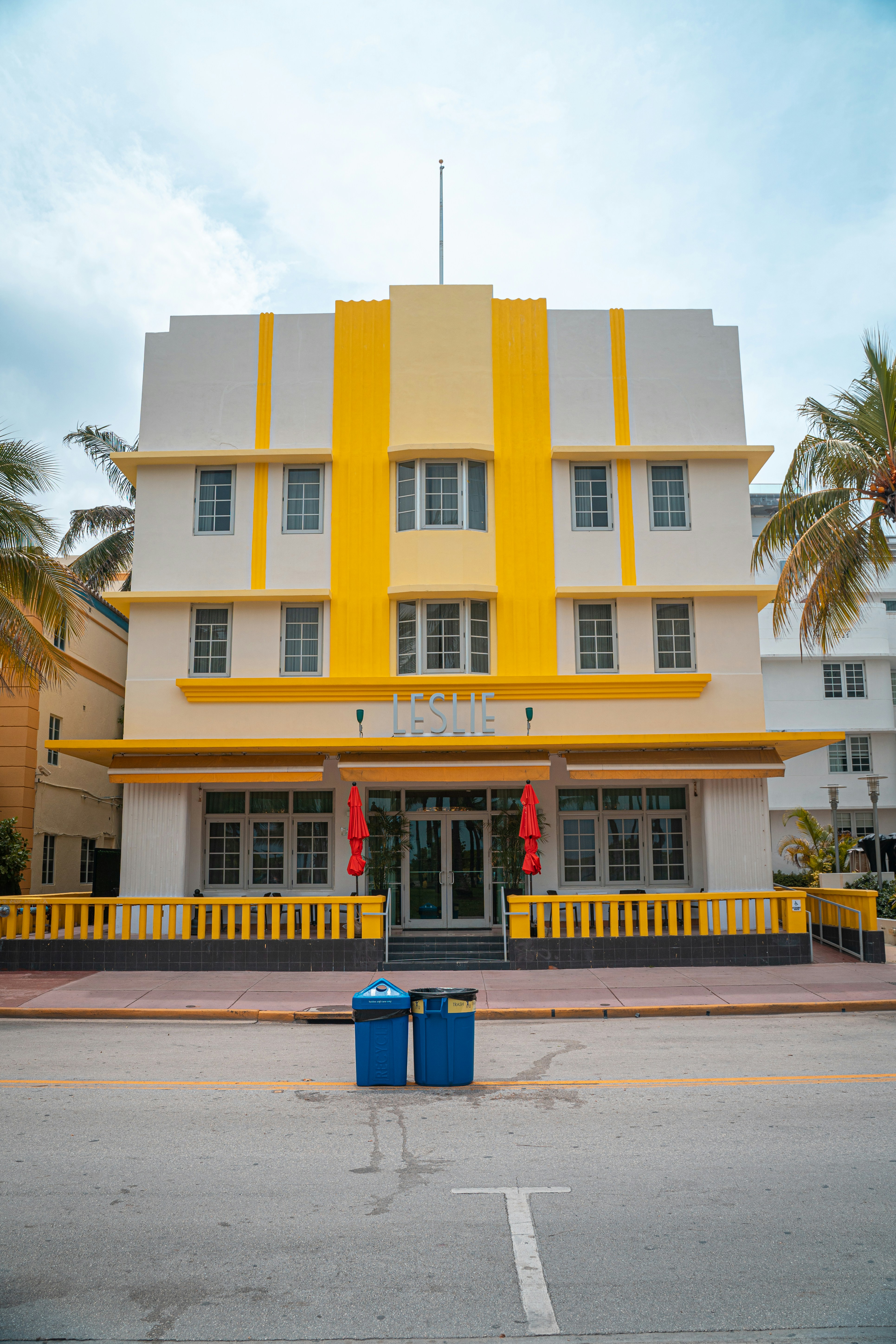 a yellow and white building with a blue trash can in front of it