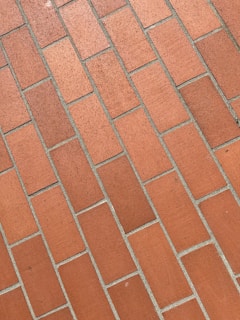 An image of a brick wall with an array of rectangular, burnt orange bricks arranged in a staggered pattern. The bricks have a slightly rough texture, and light gray mortar outlines each brick, emphasizing the geometric pattern.