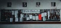 A bulletin board dedicated to World Poetry Day is adorned with various poems, some typed and others handwritten, pinned onto a dark fabric. Several framed portraits hang above the board. Dry leaves and twigs are arranged on each side of the board, adding an artistic touch.