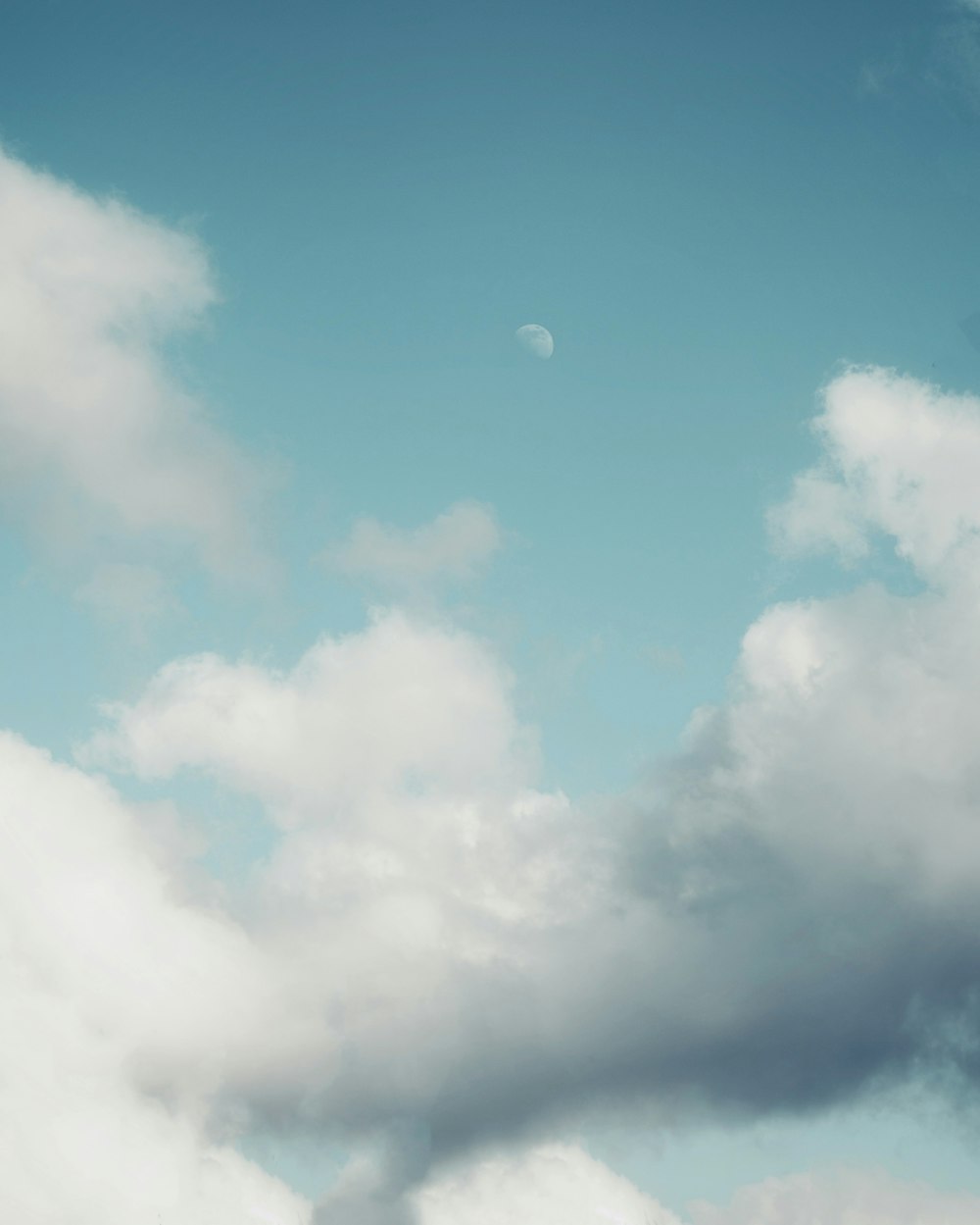 a plane flying through a cloudy sky with a half moon in the distance