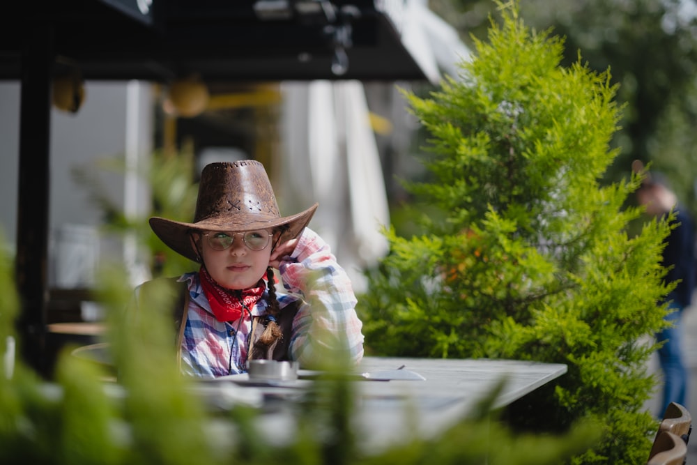 a little boy wearing a cowboy hat sitting at a table